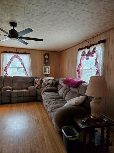 living room featuring ceiling fan, wood-type flooring, and wooden walls