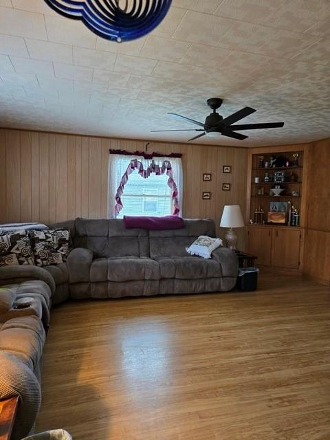 living room featuring ceiling fan, hardwood / wood-style flooring, and wooden walls