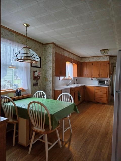 kitchen with light hardwood / wood-style flooring, sink, pendant lighting, stainless steel fridge, and ornamental molding