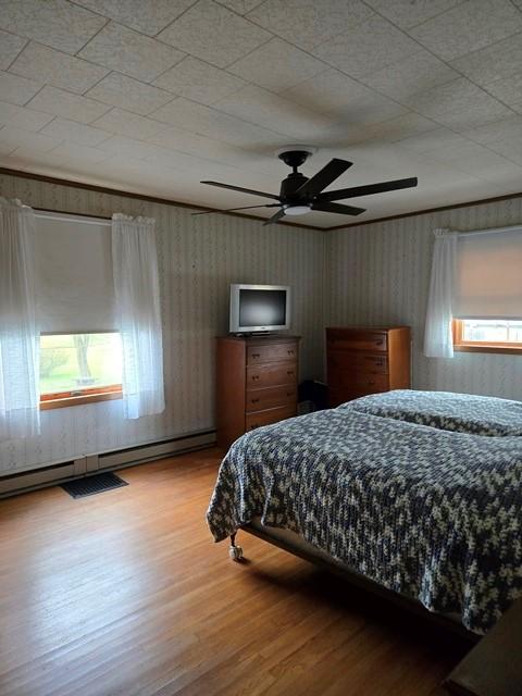 bedroom featuring a baseboard heating unit, ceiling fan, and wood-type flooring