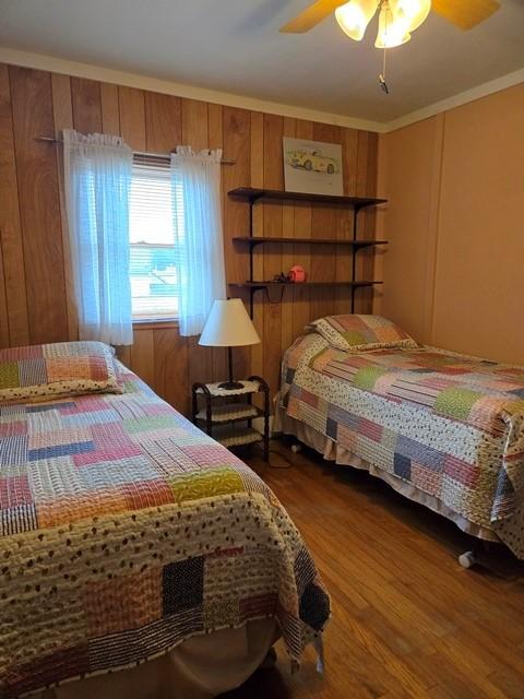 bedroom with hardwood / wood-style floors, ceiling fan, crown molding, and wooden walls