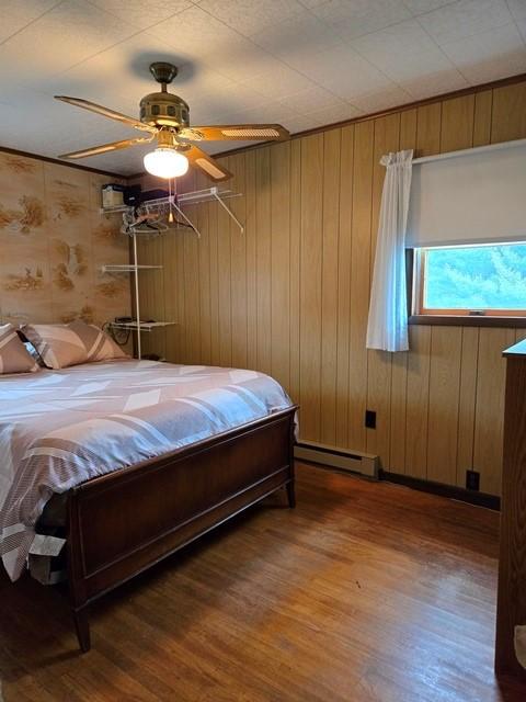 bedroom with a baseboard heating unit, ceiling fan, and wood-type flooring