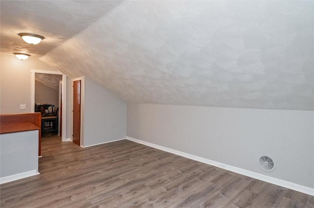 additional living space with lofted ceiling, dark wood-type flooring, and a textured ceiling