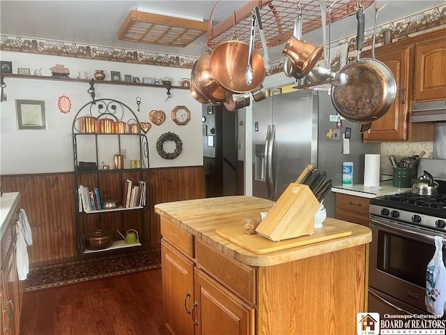 kitchen featuring dark wood-type flooring, a center island, appliances with stainless steel finishes, wooden walls, and decorative backsplash