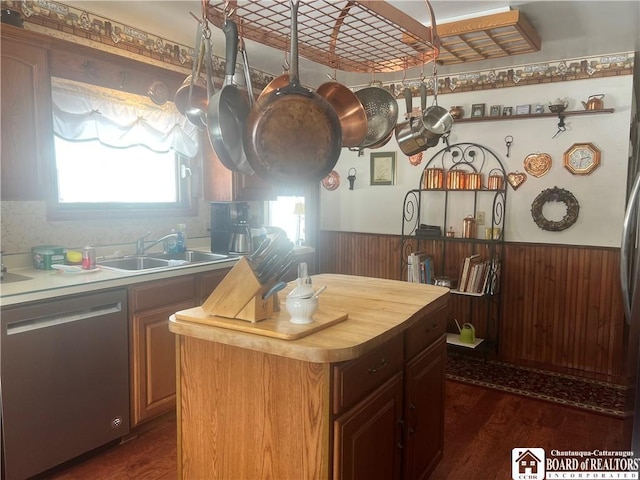 kitchen featuring stainless steel dishwasher, sink, a kitchen island, and wood walls