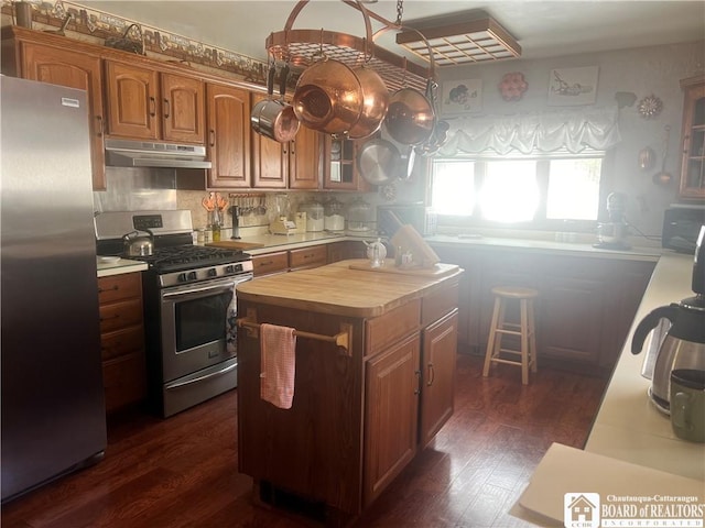 kitchen with dark wood-type flooring, backsplash, stainless steel appliances, a kitchen island, and wood counters