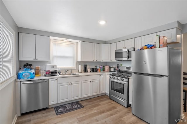 kitchen with appliances with stainless steel finishes, light hardwood / wood-style floors, sink, and white cabinets