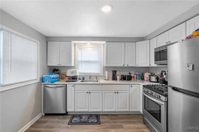 kitchen featuring stainless steel appliances, white cabinetry, sink, and light wood-type flooring