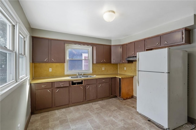 kitchen with white refrigerator, sink, backsplash, and dark brown cabinetry