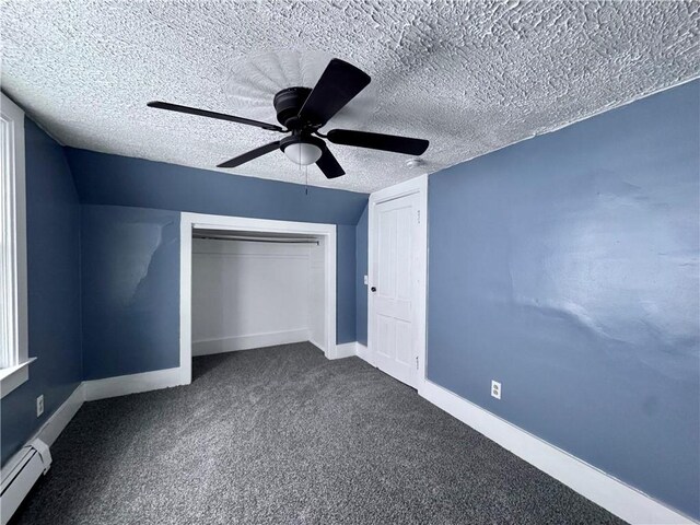 unfurnished bedroom featuring ceiling fan, dark carpet, baseboard heating, a textured ceiling, and a closet