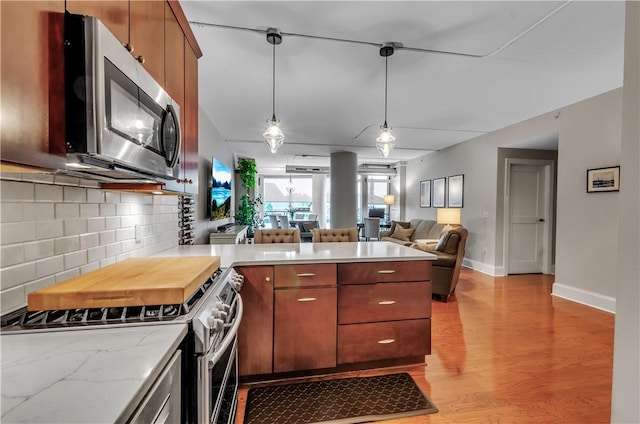 kitchen with pendant lighting, stainless steel appliances, tasteful backsplash, kitchen peninsula, and light wood-type flooring