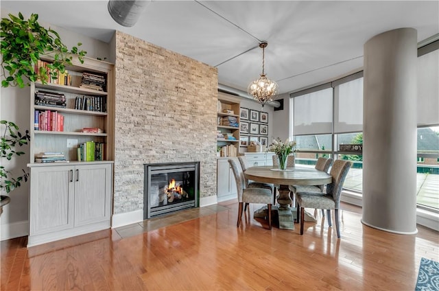 dining area featuring a stone fireplace, hardwood / wood-style floors, and an inviting chandelier