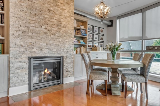 dining room featuring hardwood / wood-style flooring, a stone fireplace, and a notable chandelier