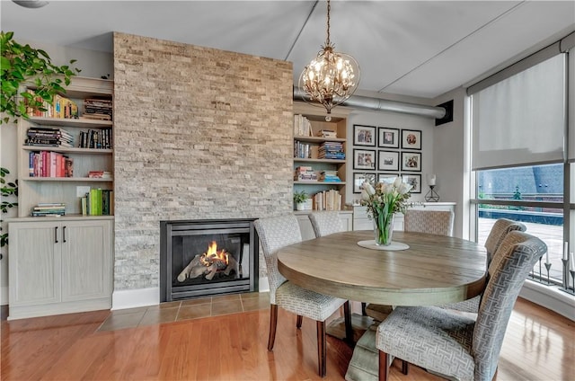 dining space with hardwood / wood-style flooring, a stone fireplace, and a notable chandelier