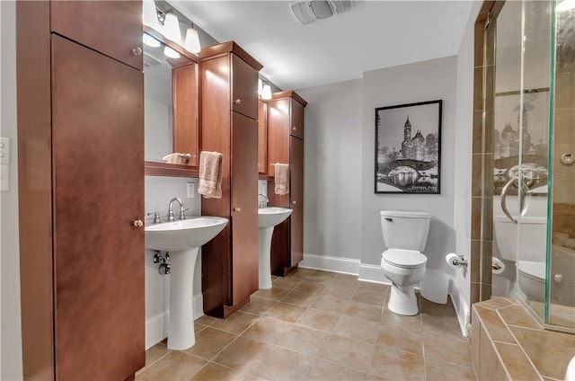 bathroom featuring tile patterned flooring, tiled shower, sink, and toilet