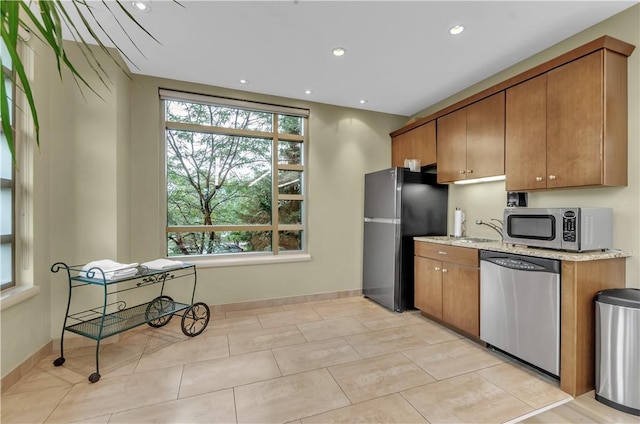 kitchen featuring sink, plenty of natural light, light stone countertops, and appliances with stainless steel finishes