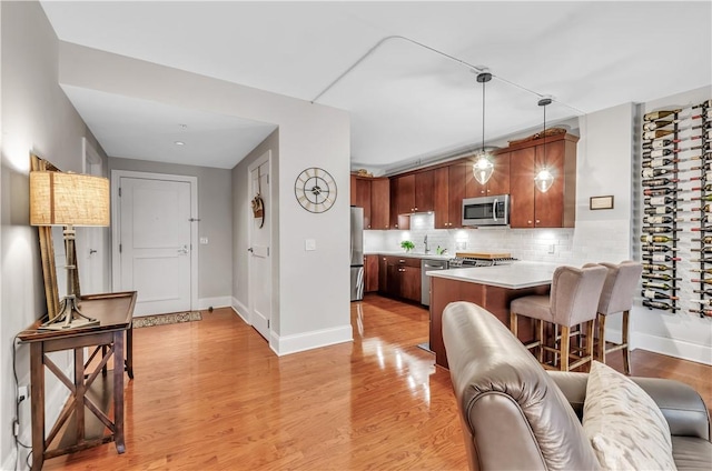 kitchen featuring pendant lighting, light hardwood / wood-style flooring, backsplash, stainless steel appliances, and kitchen peninsula