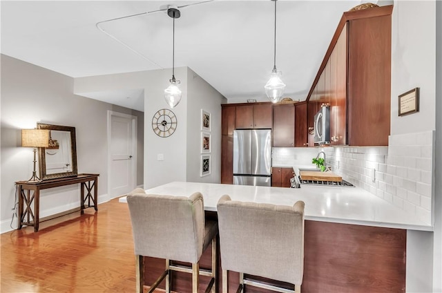 kitchen featuring a breakfast bar area, backsplash, kitchen peninsula, stainless steel appliances, and light wood-type flooring