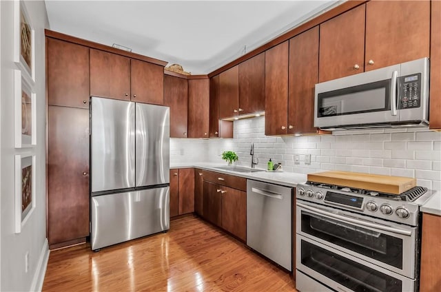 kitchen featuring tasteful backsplash, stainless steel appliances, sink, and light hardwood / wood-style flooring