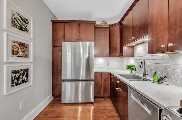 kitchen with sink, light hardwood / wood-style flooring, stainless steel appliances, light stone countertops, and decorative backsplash