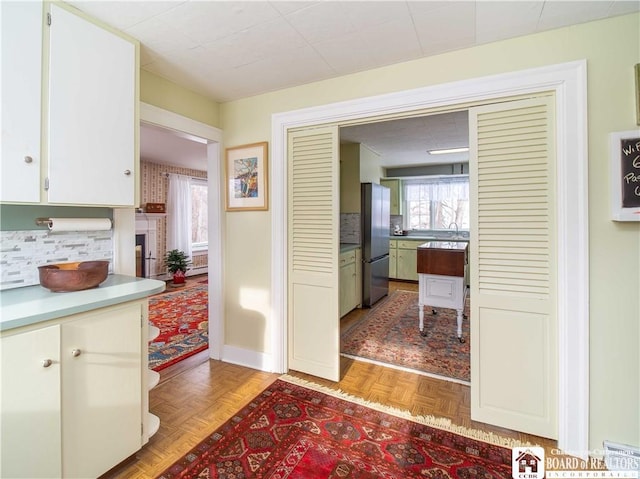 kitchen featuring light parquet floors, white cabinetry, stainless steel fridge, and backsplash