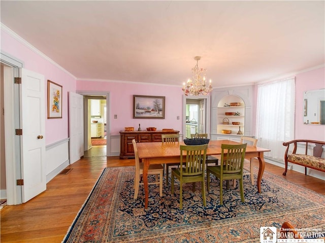 dining area with a healthy amount of sunlight, ornamental molding, light hardwood / wood-style flooring, and a notable chandelier