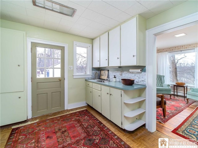 kitchen featuring white cabinetry, sink, parquet floors, and backsplash