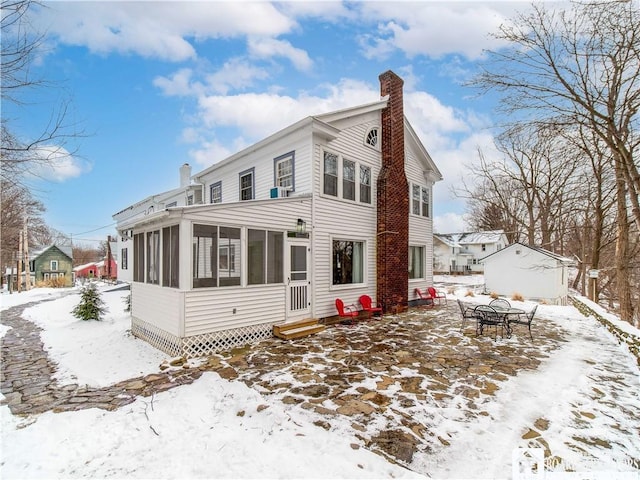 snow covered back of property with a sunroom