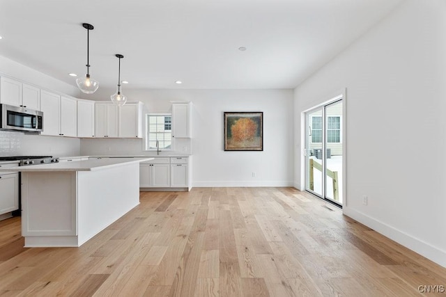 kitchen with white cabinetry, light countertops, a center island, stainless steel microwave, and pendant lighting