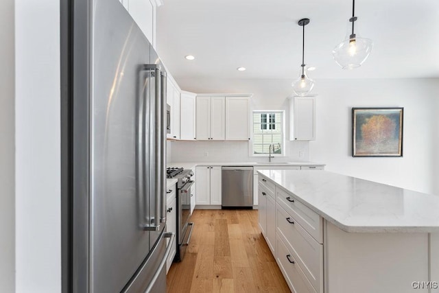 kitchen featuring light stone counters, pendant lighting, appliances with stainless steel finishes, white cabinets, and light wood-type flooring