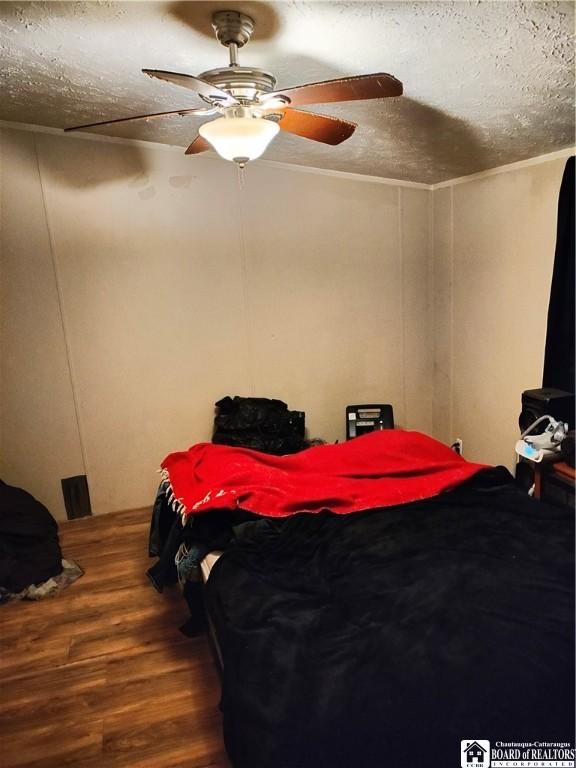 bedroom with ceiling fan, wood-type flooring, and a textured ceiling