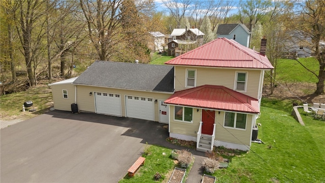view of front of property featuring aphalt driveway, a front yard, a chimney, metal roof, and an attached garage