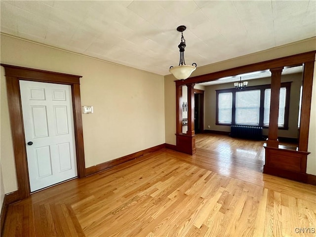 unfurnished room with decorative columns, radiator, an inviting chandelier, and light wood-type flooring