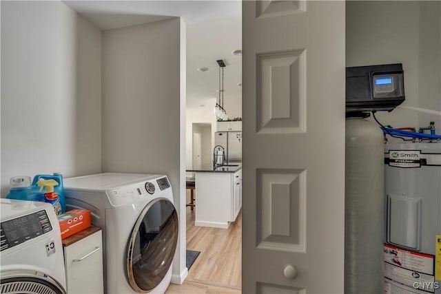 laundry area featuring washer and dryer, a sink, water heater, and light wood-type flooring