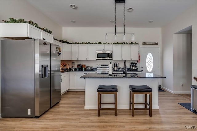 kitchen with a kitchen breakfast bar, pendant lighting, appliances with stainless steel finishes, white cabinets, and light wood-style floors