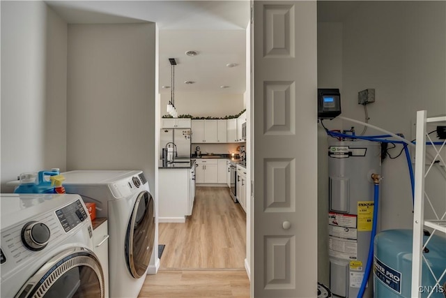 washroom featuring washing machine and clothes dryer, laundry area, a sink, light wood finished floors, and water heater