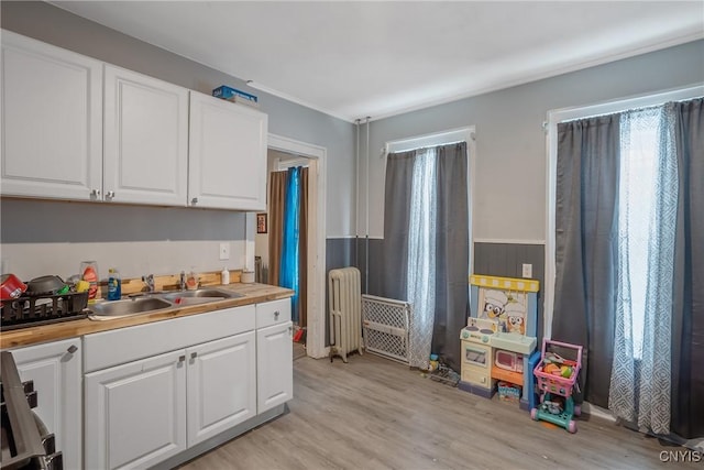 kitchen featuring white cabinetry, sink, radiator heating unit, and light hardwood / wood-style flooring