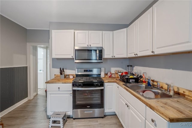 kitchen with stainless steel appliances, sink, white cabinets, and light hardwood / wood-style floors