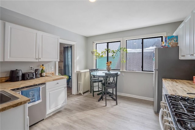 kitchen featuring butcher block countertops, light hardwood / wood-style flooring, dishwasher, white cabinetry, and radiator heating unit