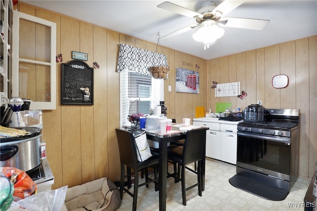 kitchen with white cabinetry, ceiling fan, wooden walls, and gas stove