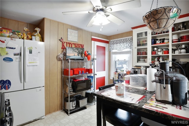 kitchen featuring white refrigerator, ceiling fan, wooden walls, and white cabinetry