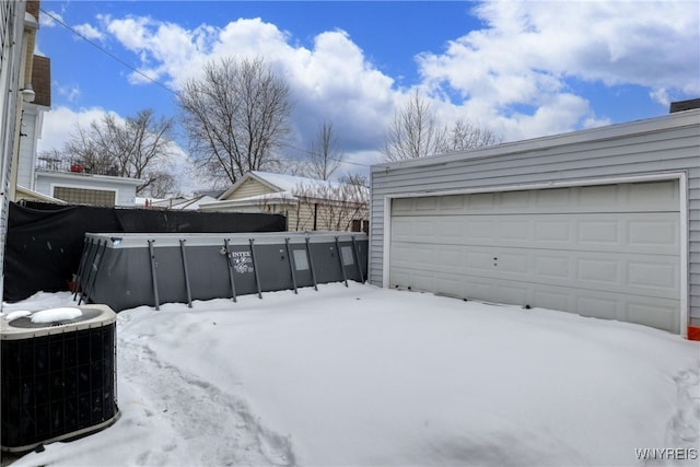 snowy yard with cooling unit, a garage, and a swimming pool