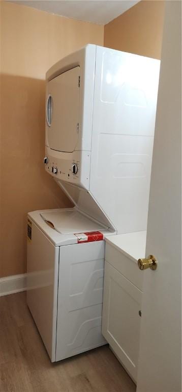 washroom with cabinets, stacked washer and clothes dryer, and light hardwood / wood-style flooring