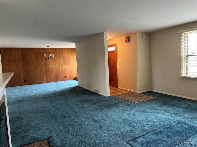 carpeted empty room with visible vents, wooden walls, and baseboards