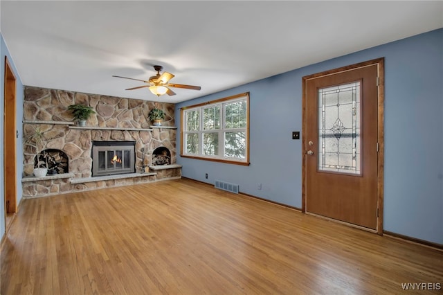 unfurnished living room with ceiling fan, wood-type flooring, and a stone fireplace