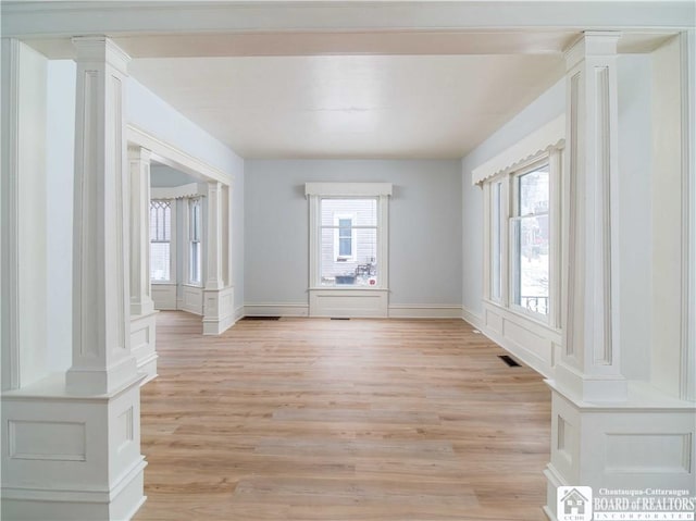 spare room featuring light hardwood / wood-style flooring, a wealth of natural light, and ornate columns