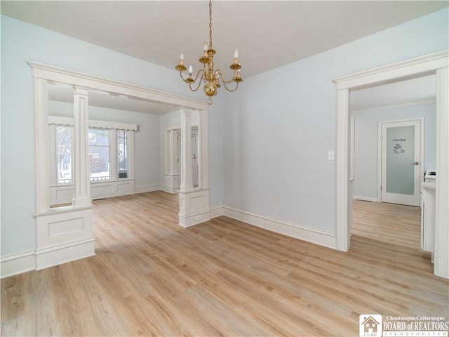 unfurnished dining area featuring ornate columns, an inviting chandelier, and light hardwood / wood-style flooring