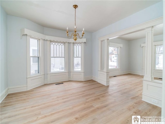 unfurnished dining area with light hardwood / wood-style flooring, a healthy amount of sunlight, and ornate columns