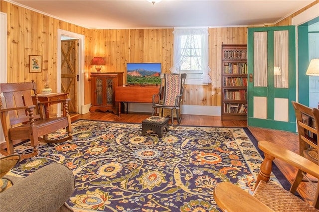 living area with crown molding, wood-type flooring, and wood walls