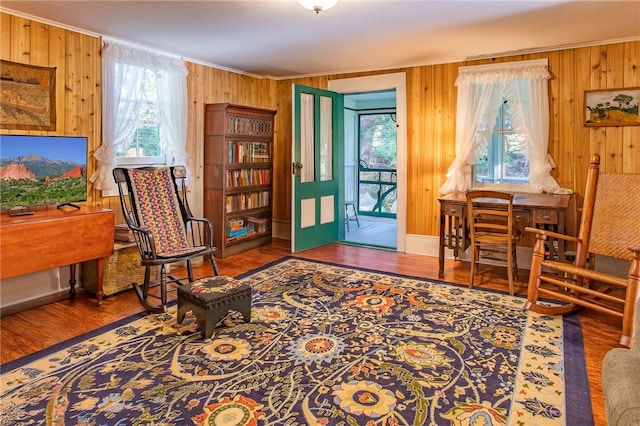 sitting room with hardwood / wood-style floors, wooden walls, and ornamental molding